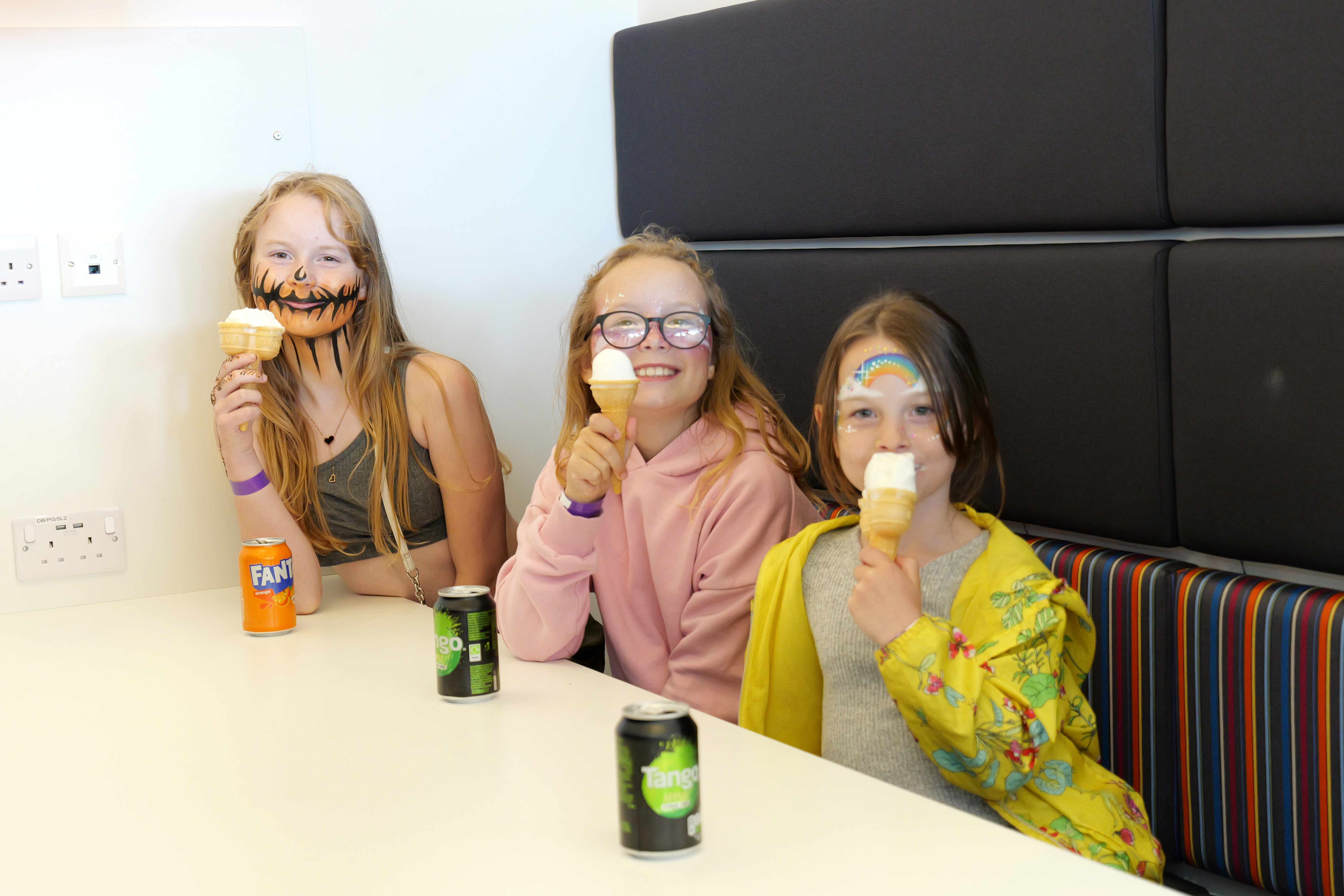 Three young girls eating ice cream with face paint on smiling at the camera