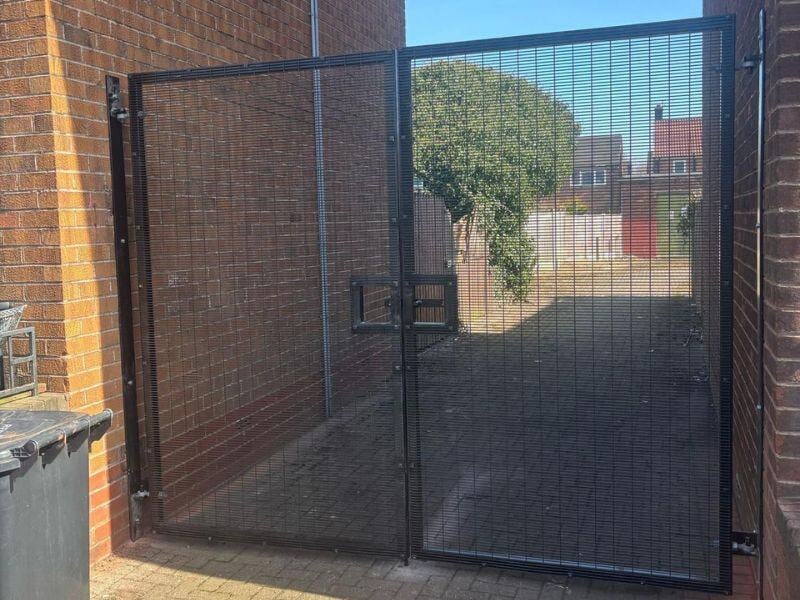 A tall black metal gate with double doors and a bolt through the middle