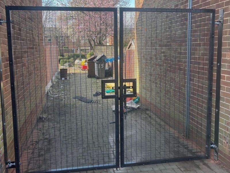 A tall black fence with double doors and a bolt through the middle