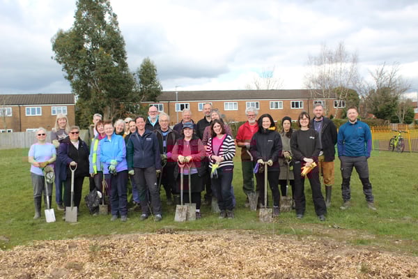 A large group of people stood smiling with spades into the ground