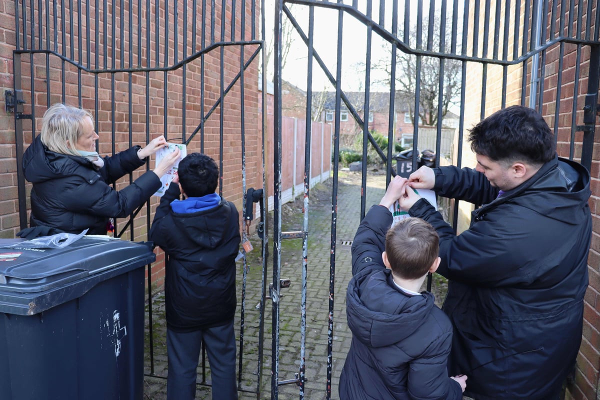 Two adults with two children hanging up hand drawn posters on a gate