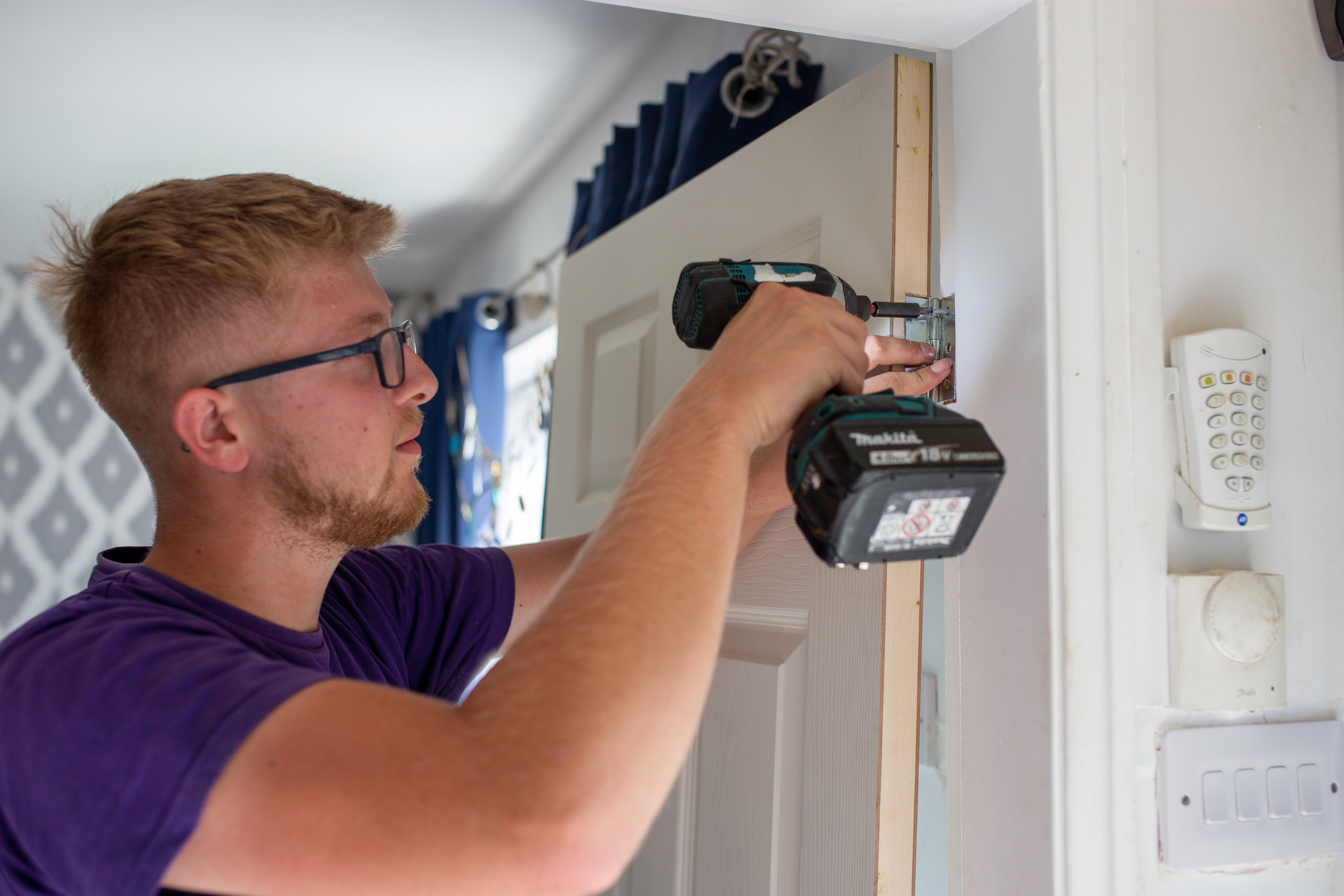 CGA employee wearing a purple t-shirt, using a drill to fix a door hinge