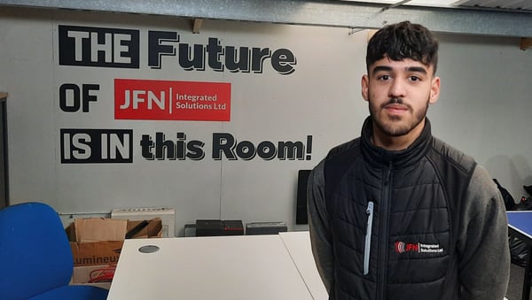 This is a photograph of Isaac Robinson stood in front of a sign which says: 'The future of JFN is in this room'.