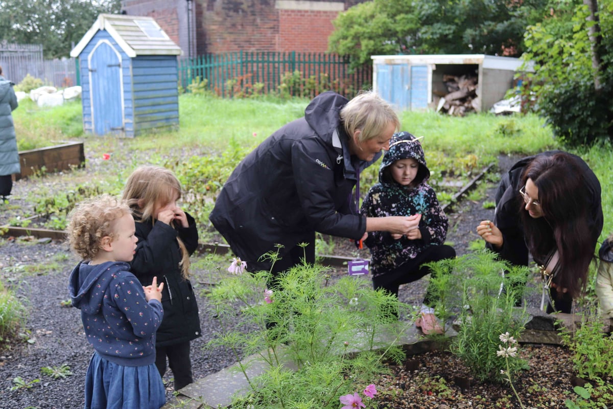 Two women and three young girls smelling the herbs from a small outdoor herb garden